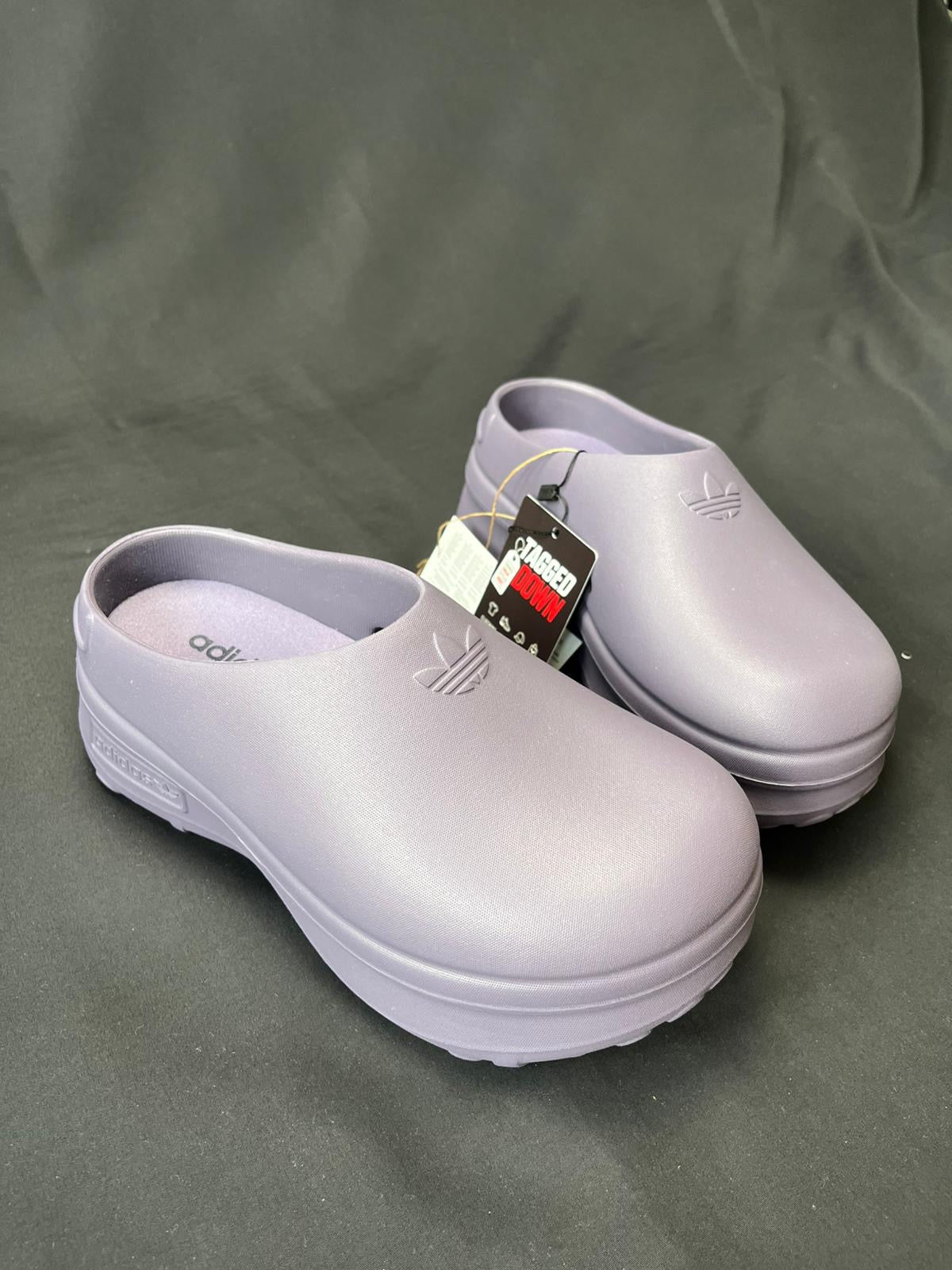 Pair of light purple clogs with a visible brand tag on a dark gray background